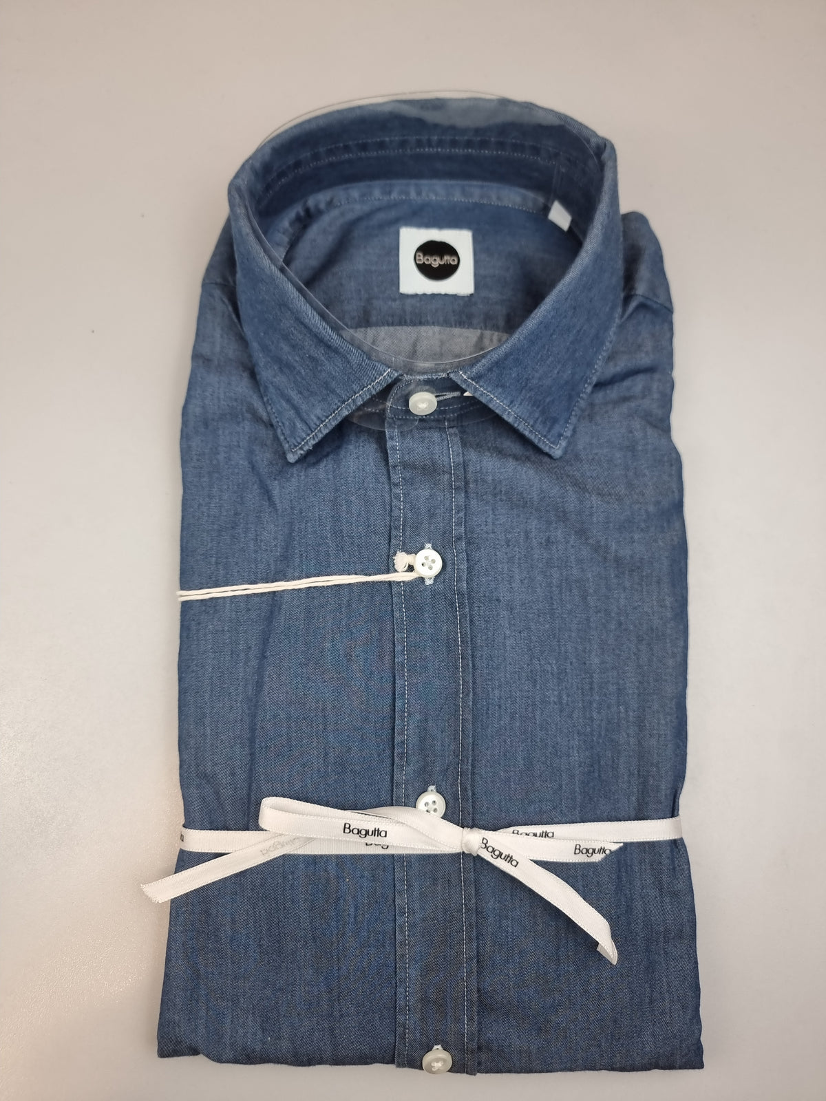 La camicia da uomo Bagutta BERLINOBJ porta il denim in un guardaroba casual curato. Realizzata in 100% cotone con vestibilità slim, abbina il collo francese all'abbottonatura con cannoncino. Le cuciture chiare a contrasto aggiungono un dettaglio distintivo alla tinta unita. Vista  piegata.