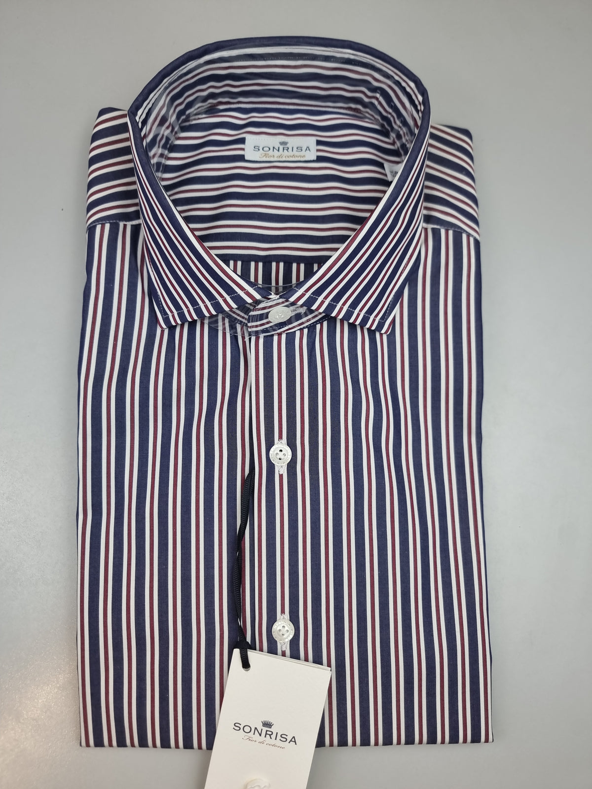 La camicia da uomo Sonrisa B878 combina righe blu, rosse e bianche in un disegno che aggiunge colore al guardaroba senza rinunciare a un look curato. Realizzata in 100% cotone, della linea Fior di Cotone e Made in Italy, presenta vestibilità classica, collo francese e polsini con bottoni. Indossa modello. Piegata