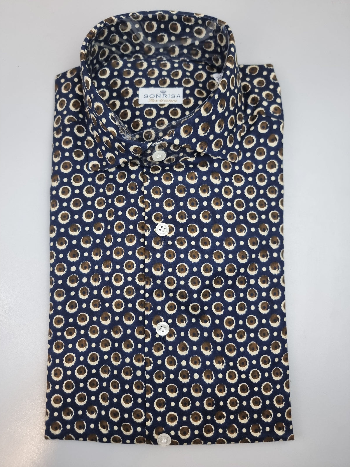 La camicia da uomo Sonrisa B878 combina il blu con dettagli di fantasia nei toni del marrone e del beige. Realizzata in 100% cotone, indicato come fior di cotone, presenta vestibilità classica, collo francese e polsini con bottoni: una proposta per dare personalità a un look curato. Vista piegata.